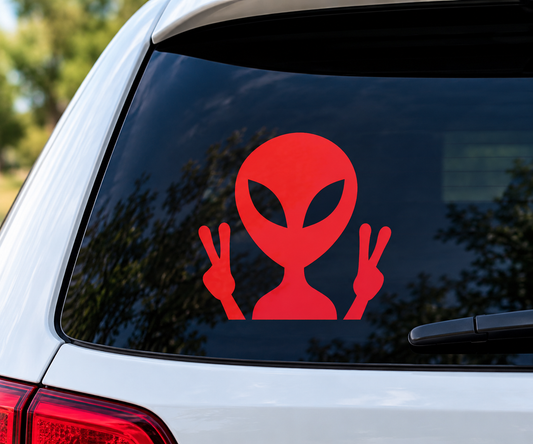 Red alien vinyl decal holding up two peace signs on a car’s rear window.