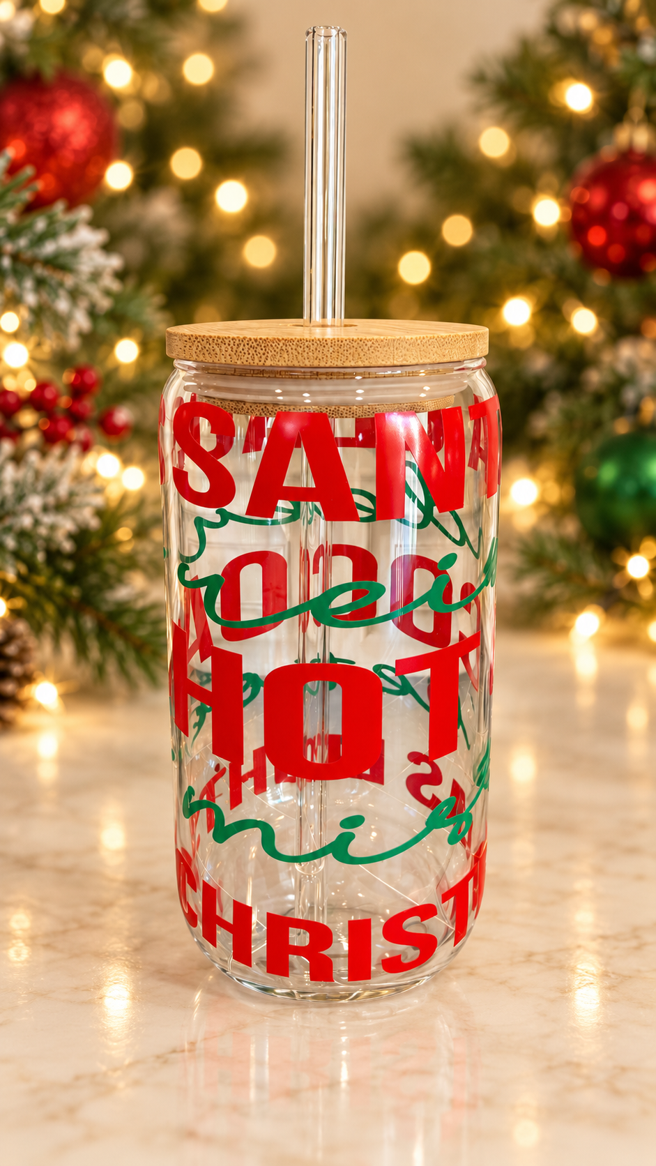 Clear glass tumbler with wraparound red Christmas block lettering and green script, topped with a bamboo lid and clear glass straw.