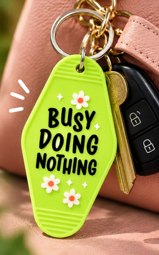 Bright green double-sided Busy Doing Nothing keychain with white daisies, sparkles, and metal key ring