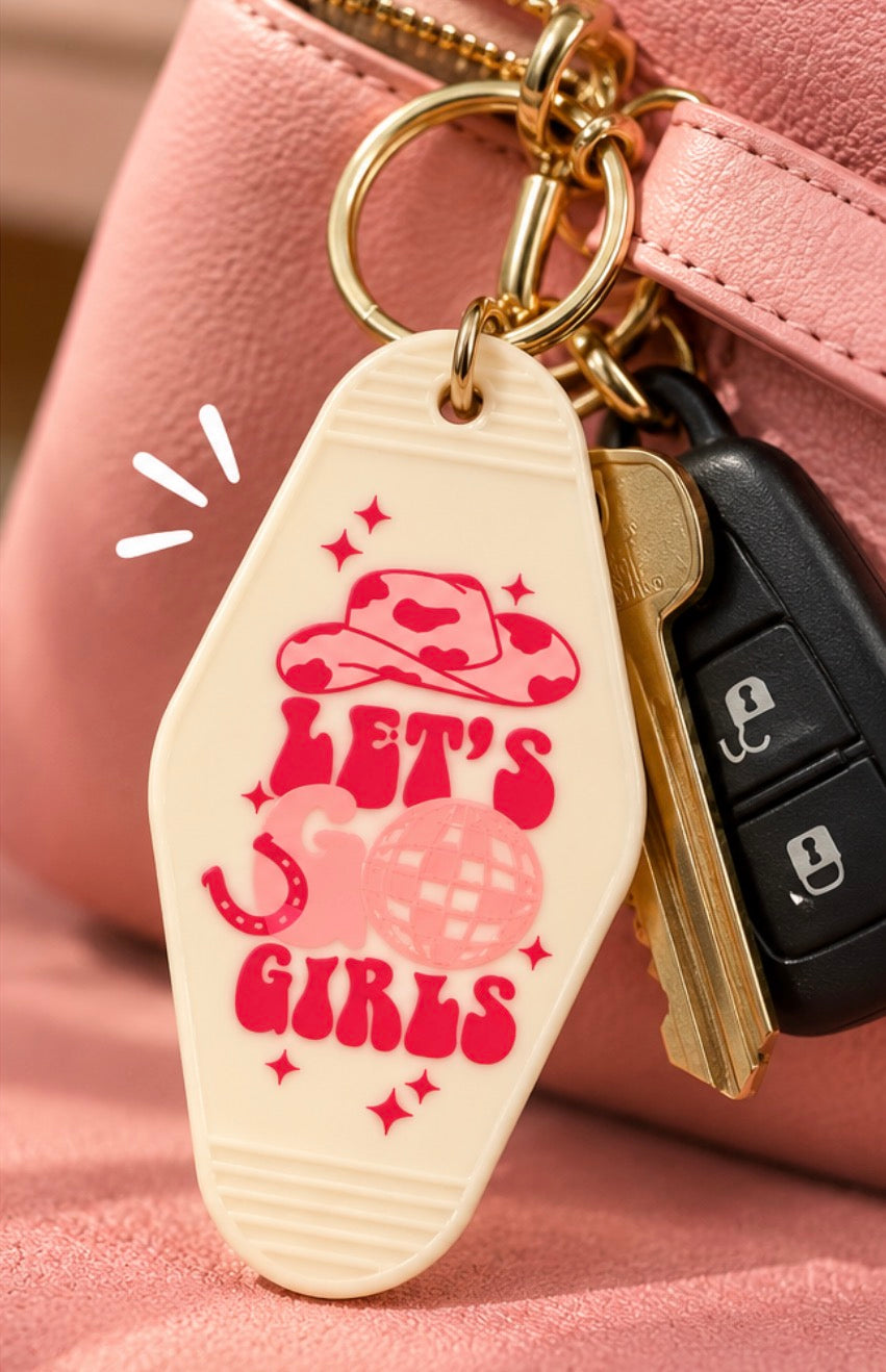 Let’s Go Girls cream motel keychain with pink cowgirl hat, horseshoe and disco ball design attached to keys and pink purse
