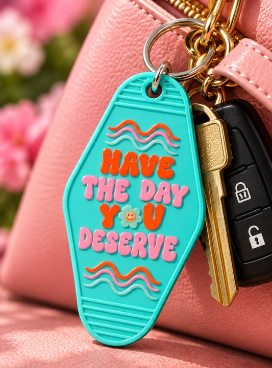 Turquoise Have the Day You Deserve motel keychain with pink and orange lettering, retro waves and smiley flower attached to keys