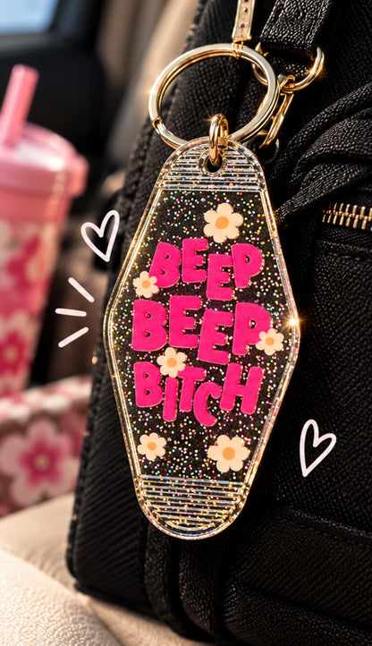 Clear glitter Beep Beep Bitch motel keychain with hot pink lettering and white daisy accents showing front and glitter back