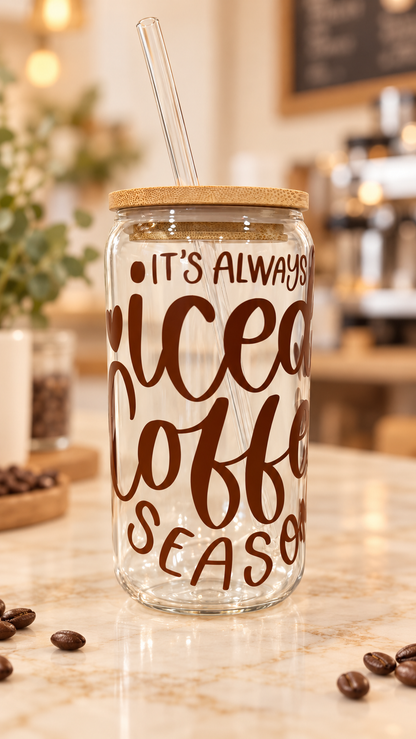 Clear glass tumbler with brown “It’s Always Iced Coffee Season” lettering and hearts, a bamboo lid, and a clear glass straw.